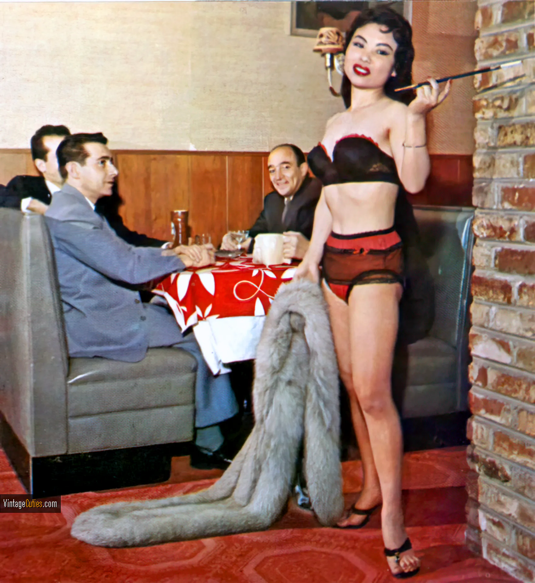 Burlesque brunette holds a long cigarette in a company of gentlemen